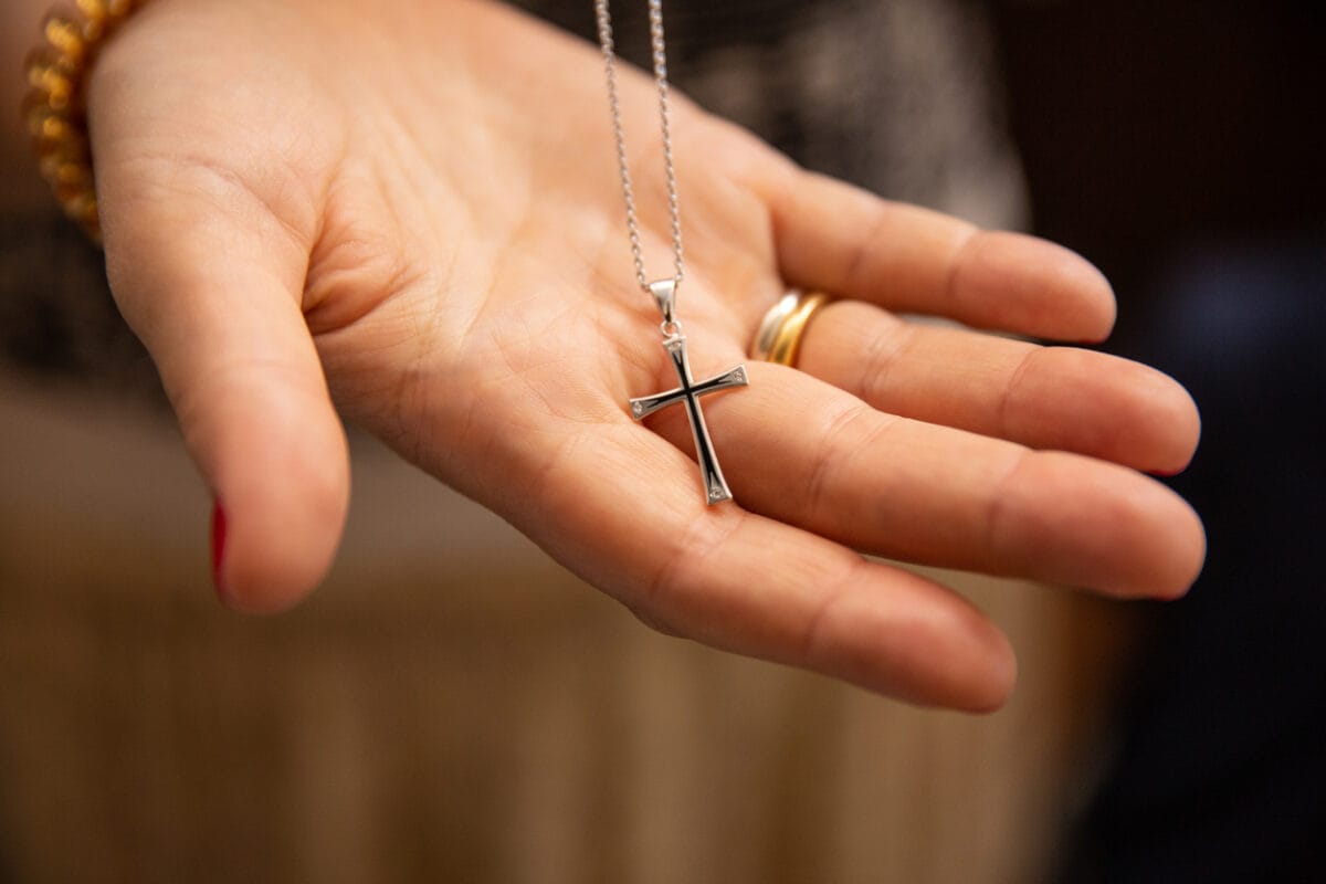 silver latin cross necklace in a hand