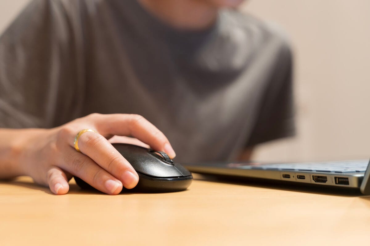 Close up hand using mouse with laptop on wooden table